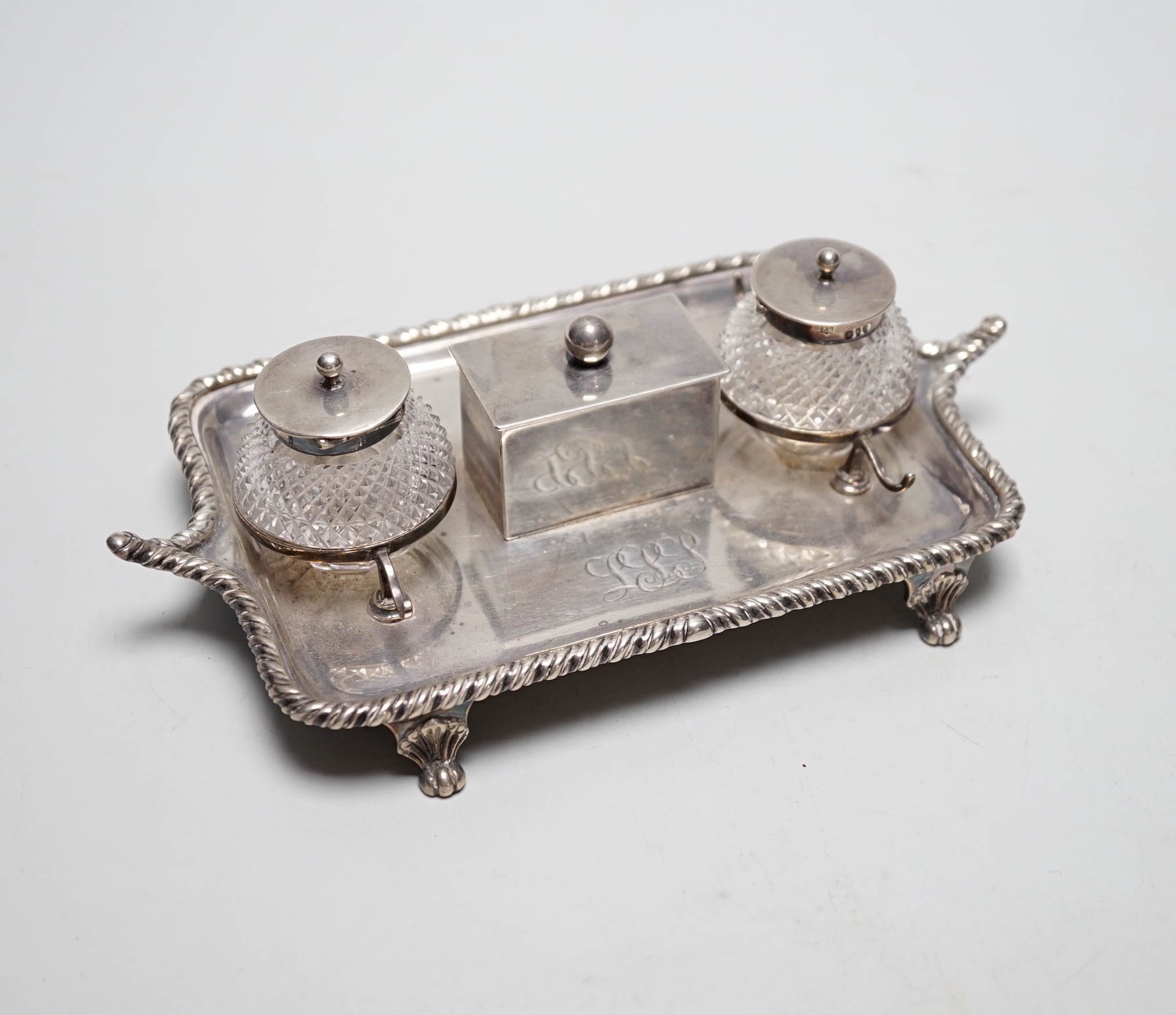 A late Victorian silver rectangular inkstand, with two mounted cut glass wells, central lidded compartment and two pen rests, Edward Hutton, London, 1890, 19cm, weighable silver 9oz.